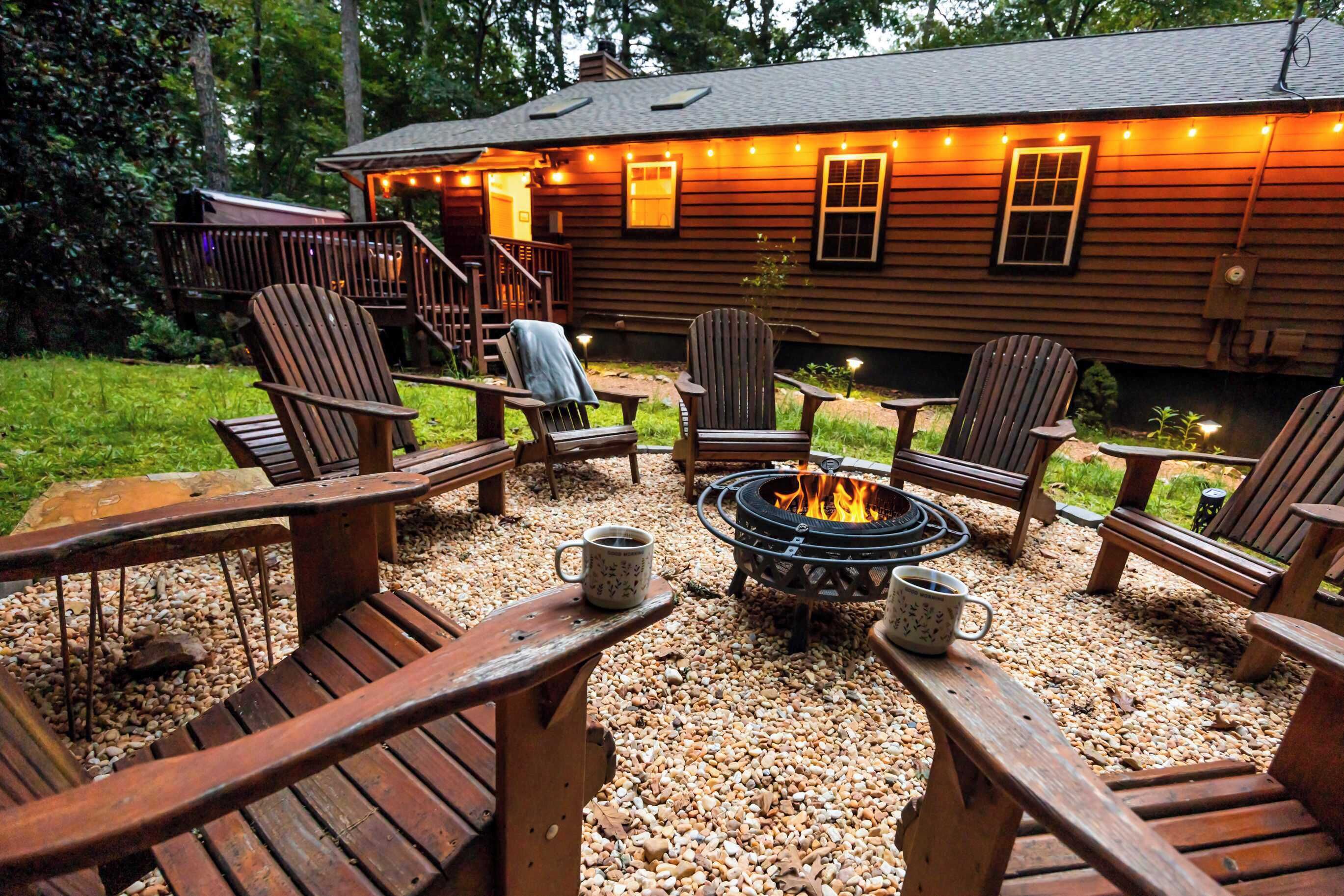 Une terrasse en bois, dotée de chaises Adirondack et d’un foyer, le tout entouré de galets.