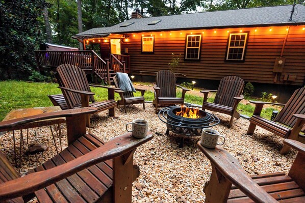 A wooden deck with Adirondack chairs and a fire pit, surrounded by pebbles.