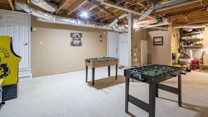 A basement with two foosball tables, exposed ductwork, and a door leading to another room. - Cozy Nest Cabin at Coosawattee (Ellijay)