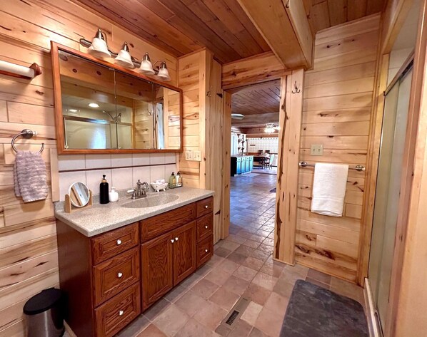 A wooden cabin interior with a bathroom featuring a large mirror, two sinks, wooden cabinets, and a tiled floor.