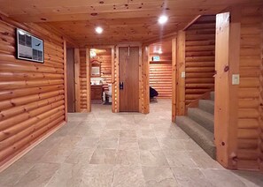 A log cabin interior with a tiled floor, wooden walls, a framed picture, and a staircase.