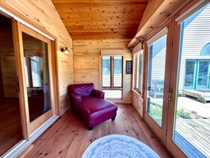 A log cabin interior with a purple sofa, large windows, and a wooden ceiling. - Serenity POW! ~ Indoor Hot Tub (WINTER ONLY)~ 3 Private Acres! (Bessemer)