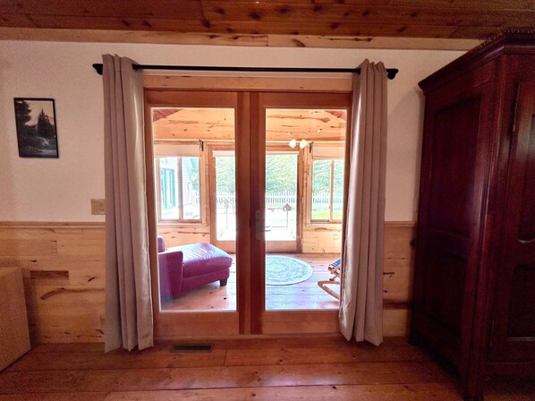 A wooden interior with a sliding glass door leading to an outdoor area with a purple sofa and a circular rug.