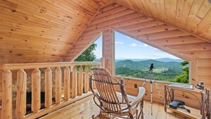Une cabane en bois dotée d’un balcon, d’une chaise berçante, d’un trépied et d’une petite table.