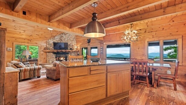 L’intérieur d’une cabane en rondins, avec une cheminée en pierre, des meubles en bois et de grandes fenêtres donnant sur les montagnes.
