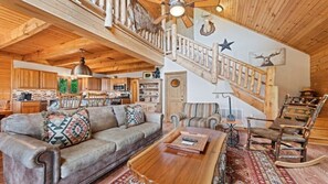 A rustic interior with a wooden staircase, a sofa, a rocking chair, and a dining area.