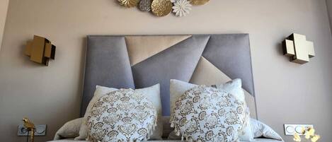 Una camera da letto con una moderna testiera, due cuscini decorati e opere d'arte a parete.