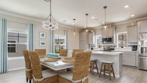 Una cocina moderna con una isla central, electrodomésticos de acero inoxidable y un comedor con sillas de mimbre.
