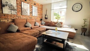 A living room with a brick wall, a sofa, a coffee table, a clock, and a guitar.