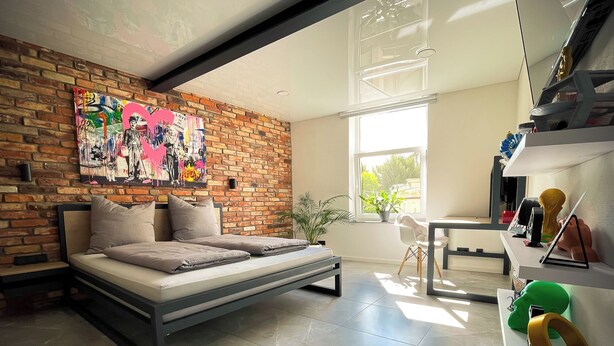 A modern bedroom with a brick wall, a bed, a desk, and a window.