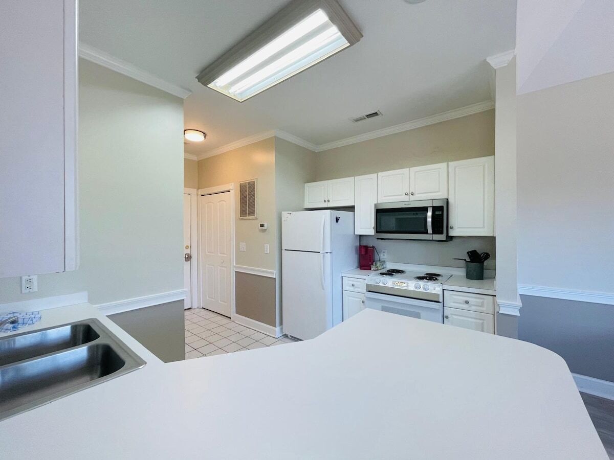 A modern kitchen with white cabinets, a stainless steel sink, a microwave, and a refrigerator.