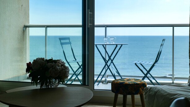 Una stanza con un balcone vista mare, un tavolo con un vaso di fiori e una sedia.