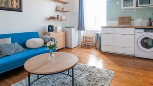 Un soggiorno moderno con un divano blu, un tavolino rotondo in legno e un angolo cucina con lavatrice.
