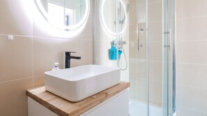 Un bagno con un lavandino bianco rettangolare, due specchi rotondi illuminati, un rubinetto nero e un box doccia in vetro.