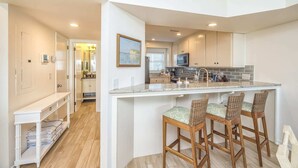 A modern kitchen with a central island, bar stools, and a view of the living area.