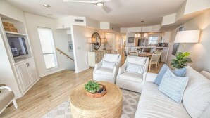 A spacious living area with a sofa, chairs, a coffee table, and a kitchen in the background.