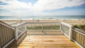 A wooden deck with a white railing overlooking a beach with people and umbrellas.