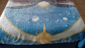 Una cama con cabecera azul, almohada a rayas rosa y blanca, y manta azul con diseño de delfín y sol.