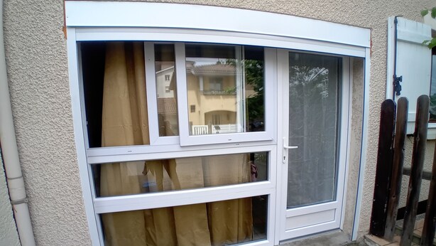 Una ventana con marco blanco y dos partes, una con cortina y otra con mosquitero.