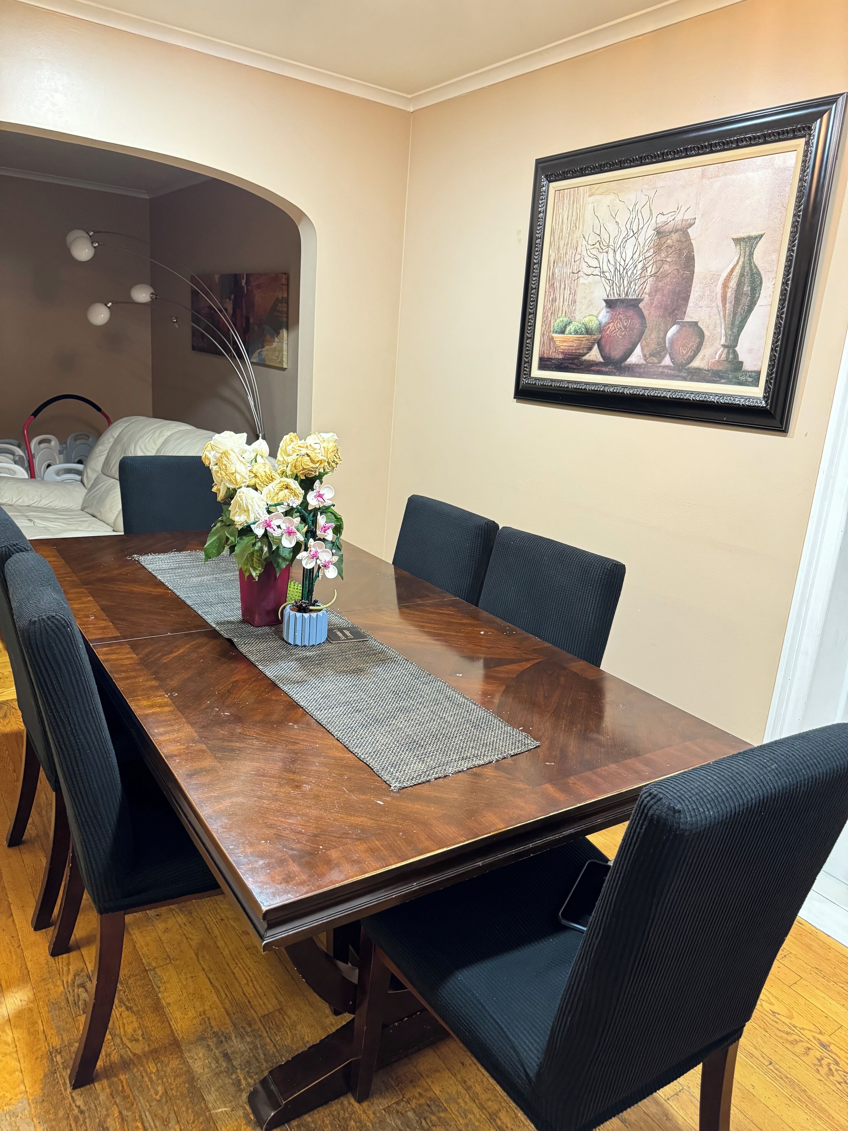 A dining area with a wooden table, black chairs, a vase of flowers, and a framed artwork on the wall.