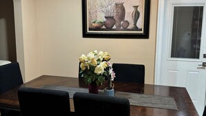 A dining room with a wooden table, black chairs, a vase of flowers, a chandelier, and a framed picture on the wall.