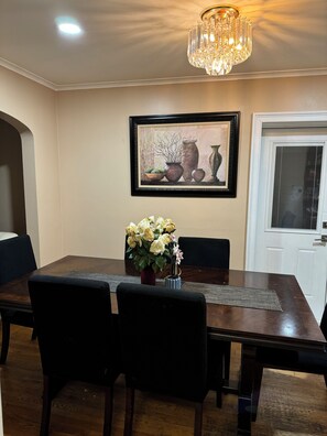 Ein Esszimmer mit Holztisch, schwarzen Stühlen, einer Blumenvase, einer Chandelierleuchtre und einem gerahmten Bild an der Wand.