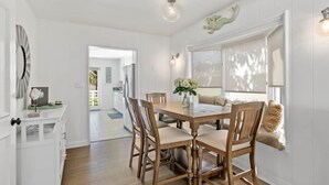 A dining area with a wooden table and chairs, a vase with flowers, and a window with a view. - Across the street from the beach with Pool and Spa (Solana Beach)