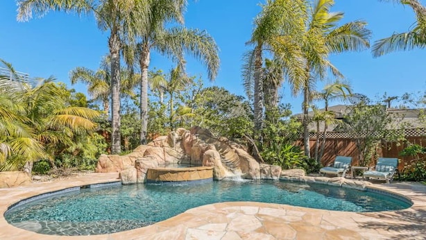 A swimming pool with a natural rock feature, surrounded by palm trees and a stone deck. - Across the street from the beach with Pool and Spa (Solana Beach)