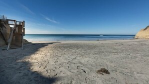 A beach with a staircase leading to a building, sandy beach, and clear blue sky. - Across the street from the beach with Pool and Spa (Solana Beach)