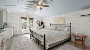 A bedroom with a bed, a ceiling fan, a small table, and a door leading to an outdoor area.