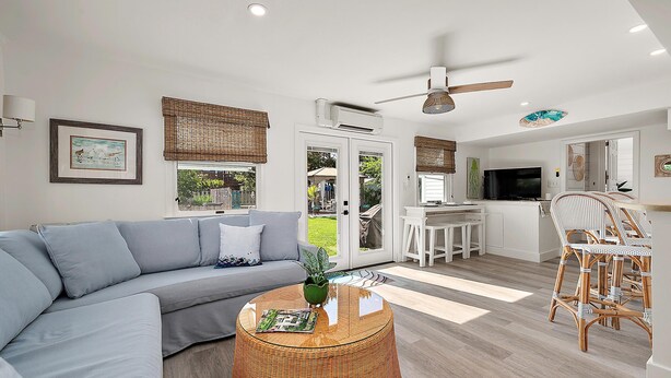 A modern living room with a grey sofa, a round wicker coffee table, and a dining area with wicker chairs.