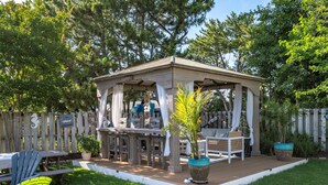 A covered outdoor seating area with a wooden deck, a table, chairs, and potted plants.