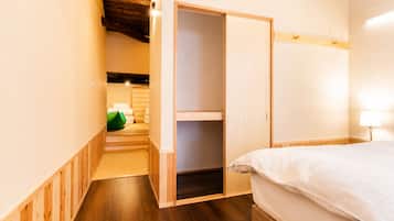 Une chambre avec un plancher en bois, un lit avec une literie blanche, une armoire et un sac vert dans un coin.