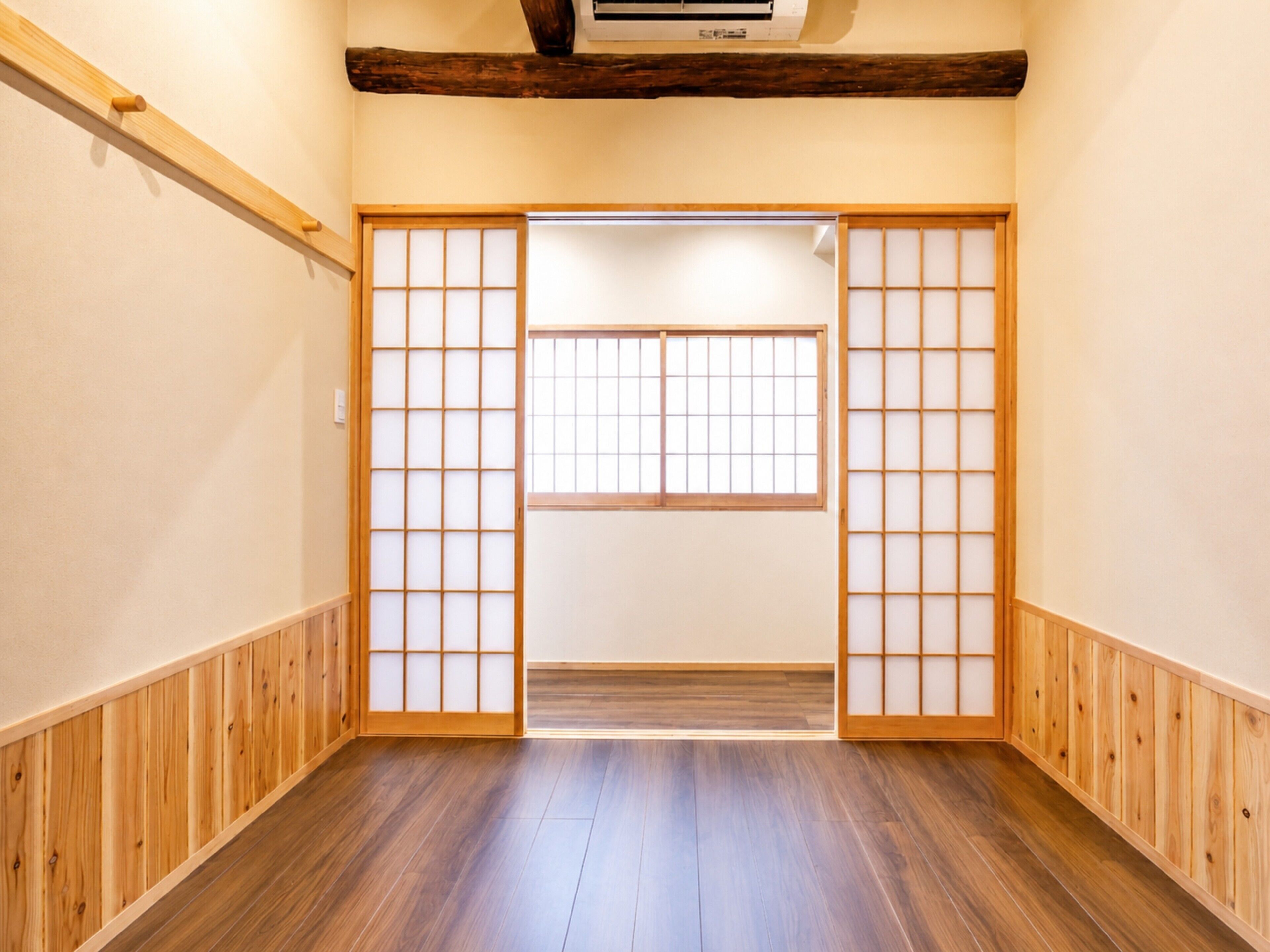 A room with wooden flooring, a sliding door with a grid pattern, and a ceiling-mounted air conditioning unit.
