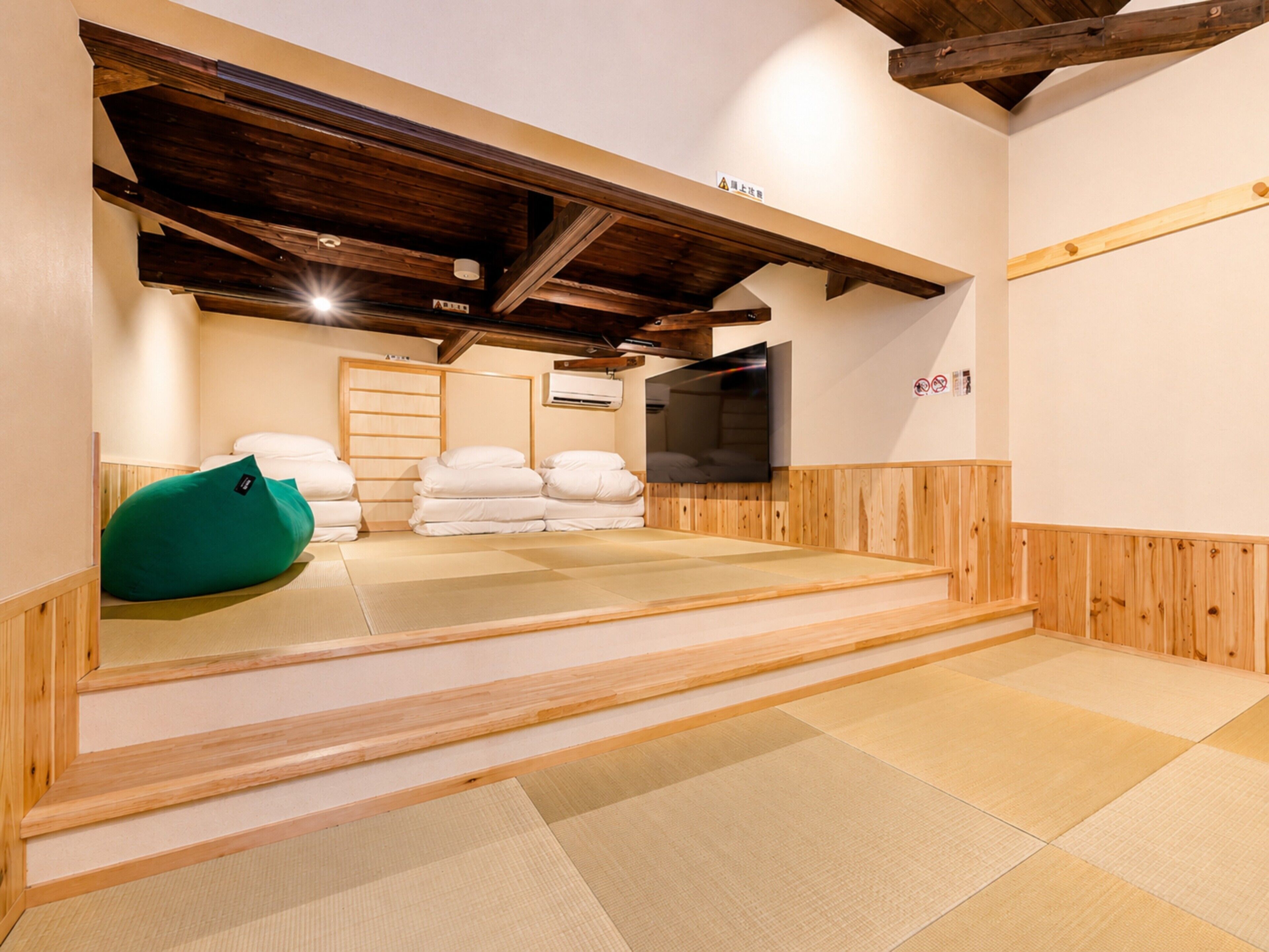 A tatami mat room with a television, pillows, and a green bean bag.