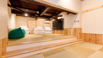 A tatami mat room with a television, pillows, and a green bean bag.