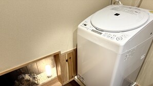 A compact, white washing machine in a corner of a room with beige walls and a wooden floor. - Nara-Ryokan  Villa West (Nara)
