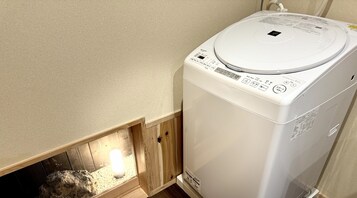 Una lavadora blanca y compacta en un rincón de una habitación con paredes beige y piso de madera.