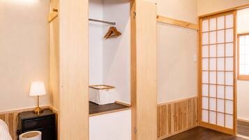 A room with a wooden wardrobe, a hanging clothes rack, a bedside table with a lamp, and a shoji screen door.