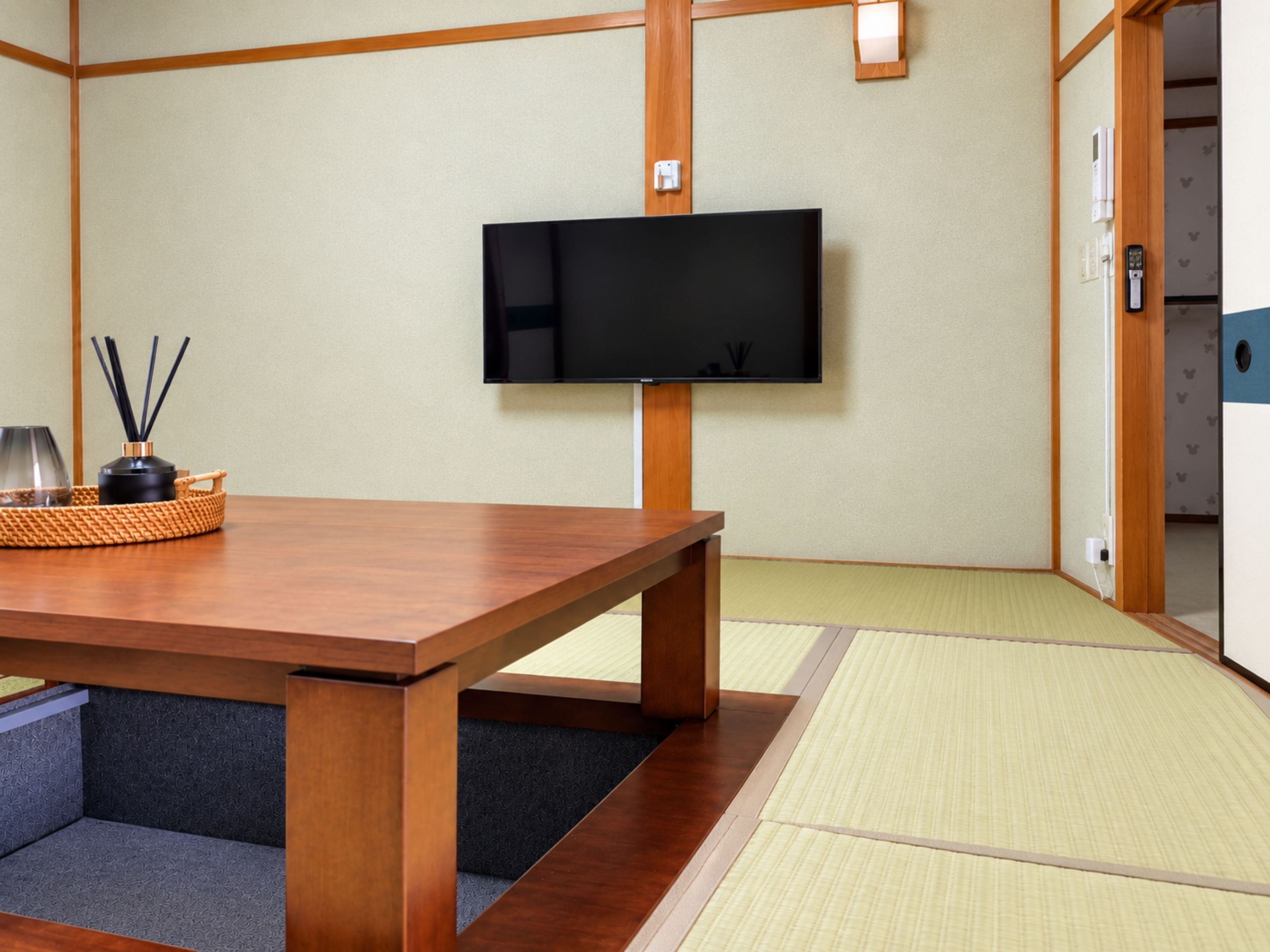 A traditional Japanese room with tatami flooring, a wooden table, a television, and a sliding door.