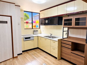 A modern kitchen with wooden cabinets, a microwave, a sink, and a window with a view of a backyard. - Nara-Ryokan Villa (Nara)