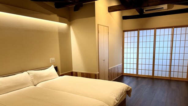 A bedroom with a bed, wooden flooring, a sliding door with frosted glass panels, and a ceiling fan. - Nara-Ryokan  Villa West (Nara)