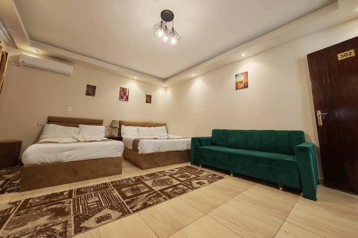 A bedroom with two beds, a green sofa, a patterned rug, and a ceiling light fixture.