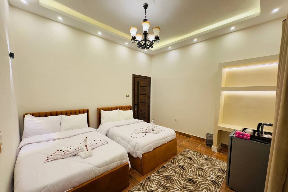 A hotel room with two beds, a zebra-patterned rug, a desk with a lamp, and a ceiling light fixture.