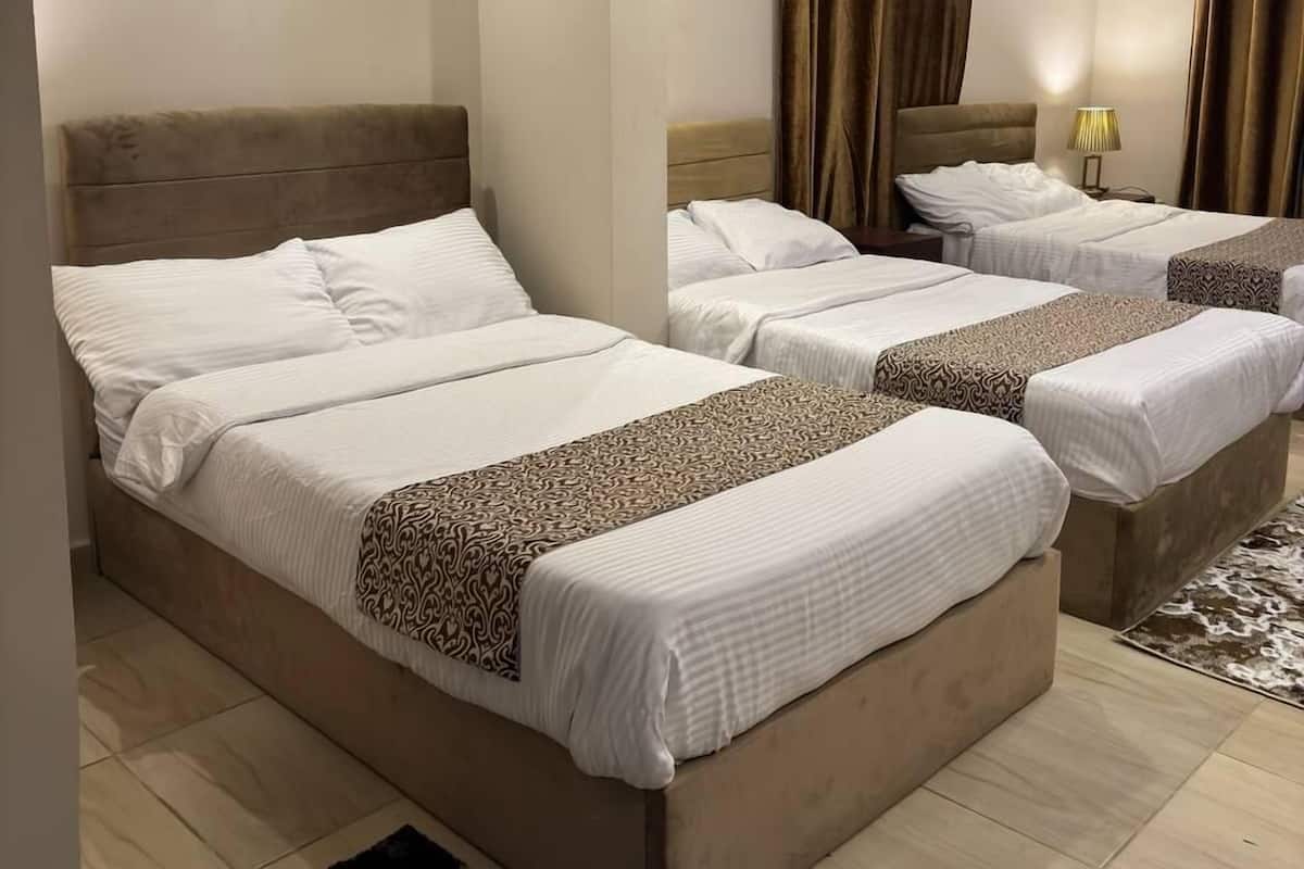 A hotel room with three beds, each with a headboard and white bedding.