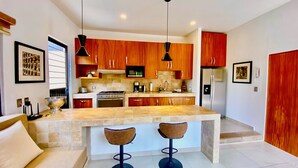 Una cocina moderna con armarios de madera, una isla central con taburetes de bar, horno empotrado y refrigerador.
