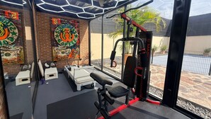 Un gimnasio con equipo de ejercicio, una banca y una pared con obras de arte coloridas.