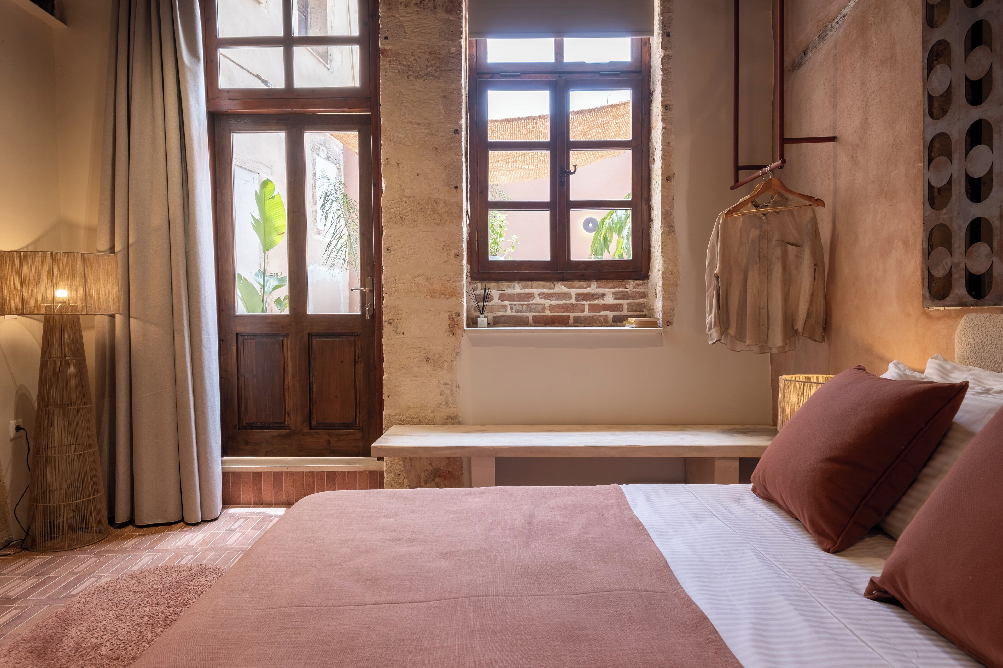 A bedroom with a large bed, a bench, a window with a view, and a hanging garment rack.