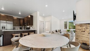 Una cocina moderna con armarios de madera oscura, un refrigerador de acero inoxidable y un comedor con una mesa de mármol y sillas de madera.