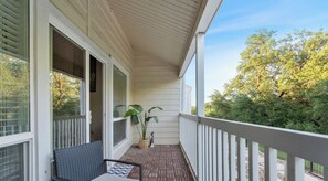 A covered porch with a wicker chair and a small table, a potted plant, and a view of trees and greenery. - Lakeshore #27 xxxxxx (Austin)